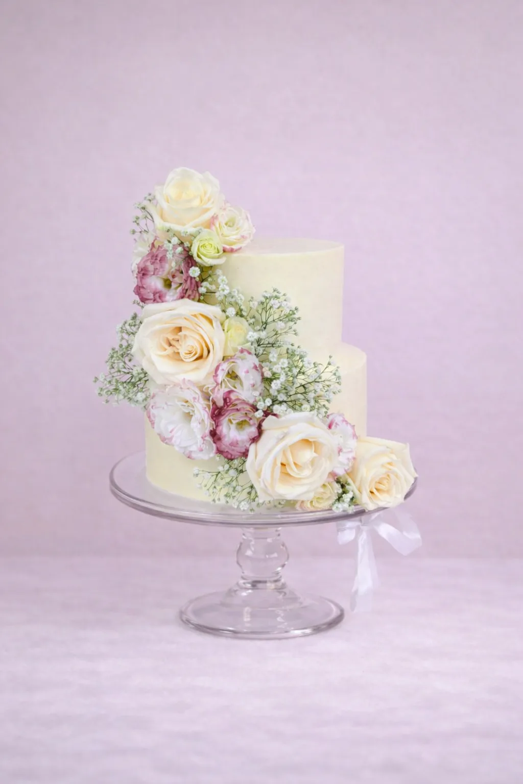 Tarta de boda de dos pisos con cascada de rosas blancas y crema, lisianthus y paniculata, estilo romántico, para bodas en Granada.